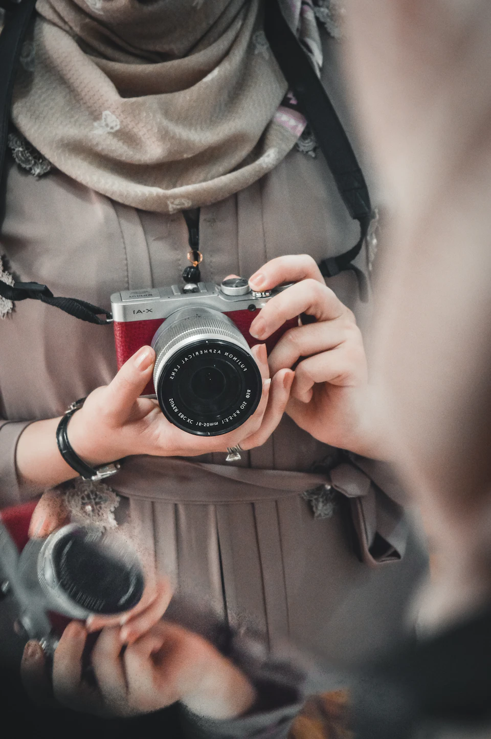 Person holds silver camera with black lens up to their face in front of blur