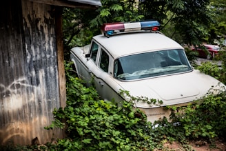 A scrap white police car parked near a house.
