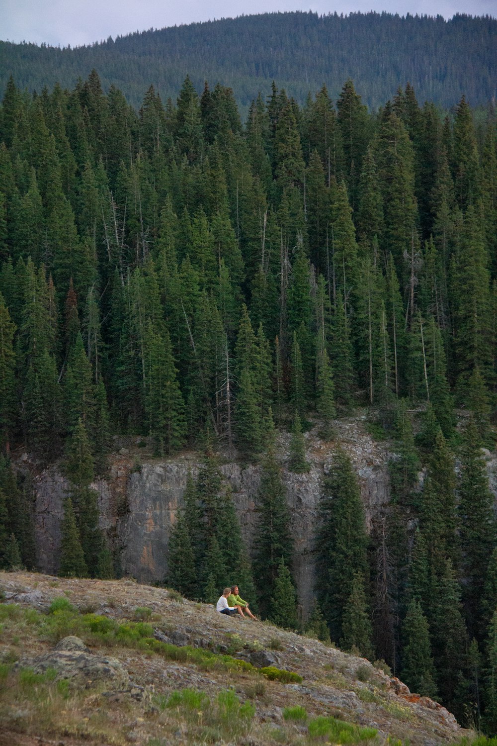 deux personnes assises sur le bord de la montagne