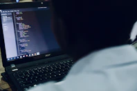 A focused student coding on a laptop with Java code on the screen