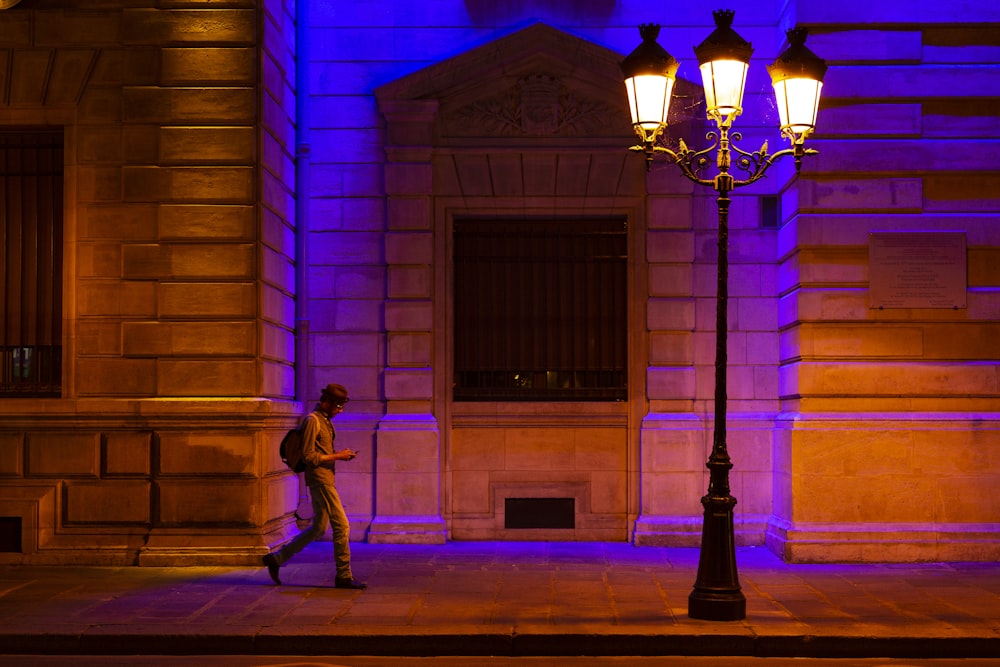man walking at sidewalk with turned on streetlight