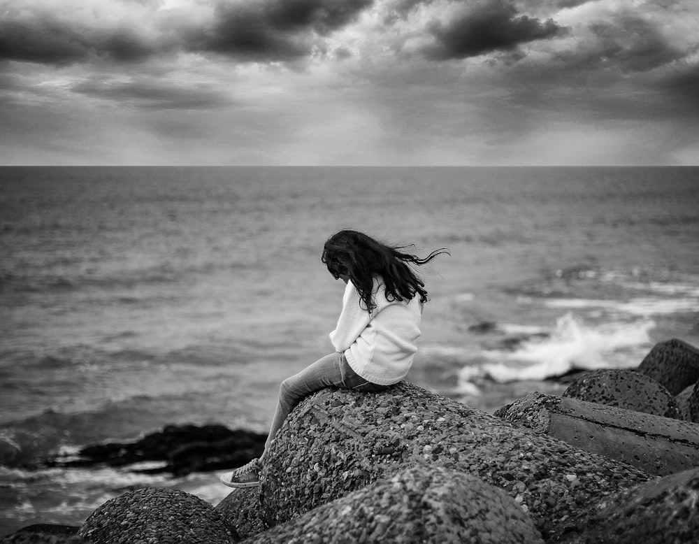 grayscale photography of woman sitting near body of water