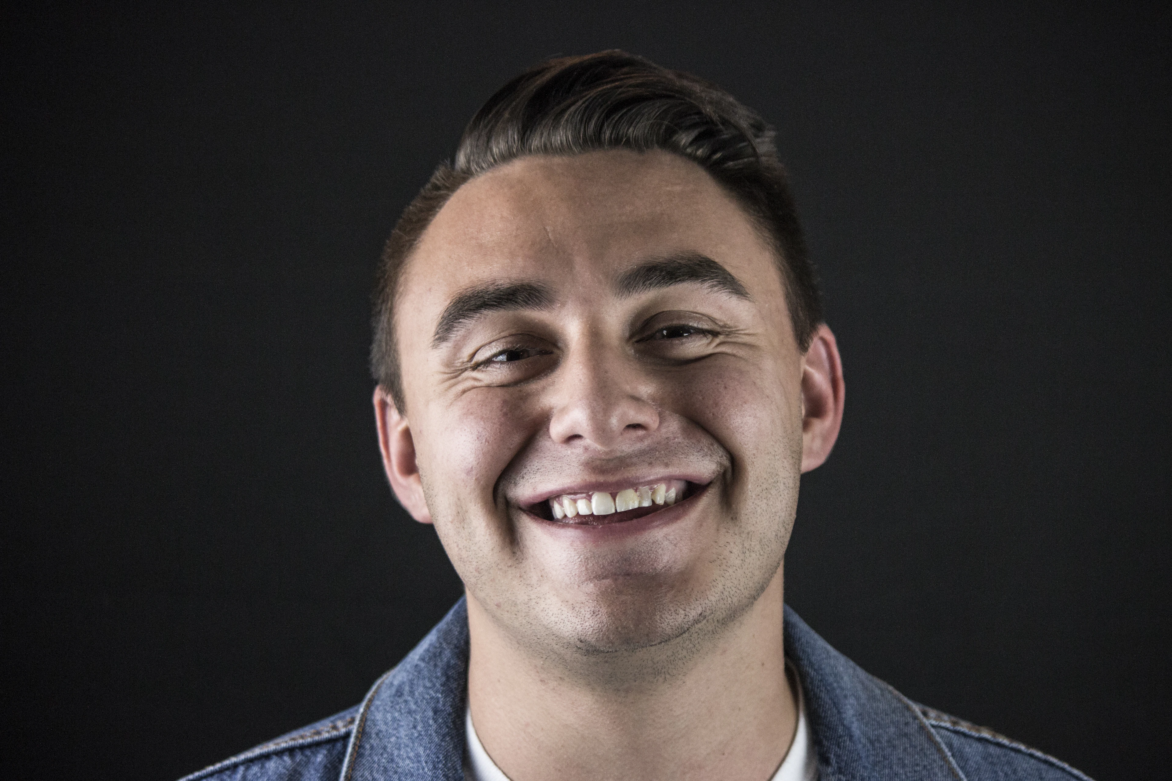 Smiling man in a denim jacket against a dark background