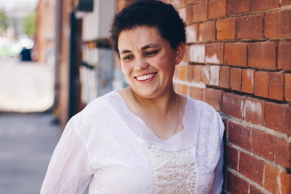 woman smiling while leaning on brick wall