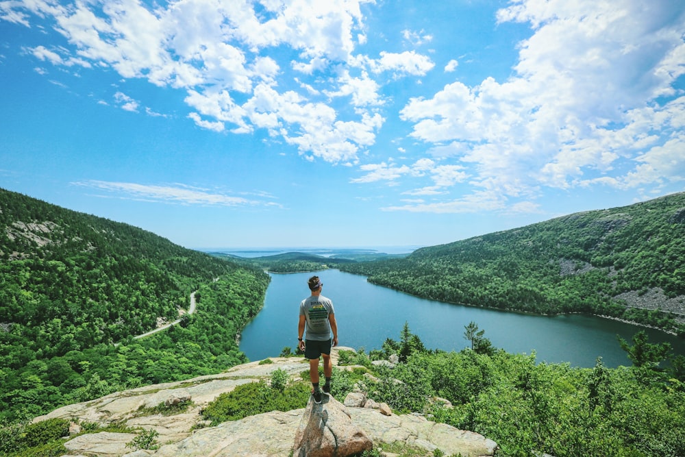 man standing on rock against lake and mountains