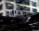 An RRTS train speeding along elevated tracks with city buildings in the background.