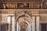An ornate interior with elaborate classical architecture, displaying detailed moldings and carvings. The ceiling features intricate frescoes and gilded decorations, while marble columns and arches frame the walls, adorned with relief sculptures.