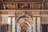 An ornate interior with elaborate classical architecture, displaying detailed moldings and carvings. The ceiling features intricate frescoes and gilded decorations, while marble columns and arches frame the walls, adorned with relief sculptures.