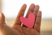 Close-up of hands holding a small, glowing heart symbolizing emotional care.