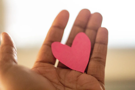 A warm image showing hands gently holding a glowing heart symbolizing care and donation.