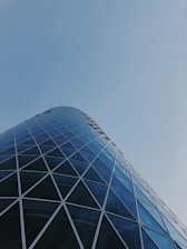 A modern skyscraper with a distinct glass and steel facade curves gracefully into the sky. The geometric diamond pattern of the windows adds a sense of complexity and elegance to the architectural design.