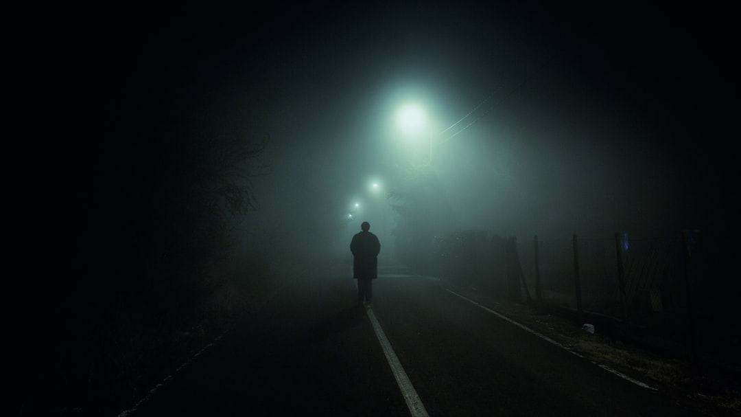 man walking at blacktop road with turned on streetlights