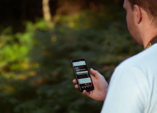 A person reading product reviews on a smartphone while enjoying a morning walk in nature.