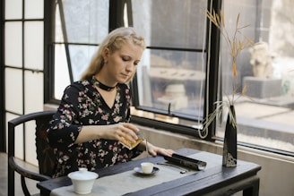 A serene woman in her 40s sitting peacefully in a sunlit room, journaling with a cup of tea nearby.