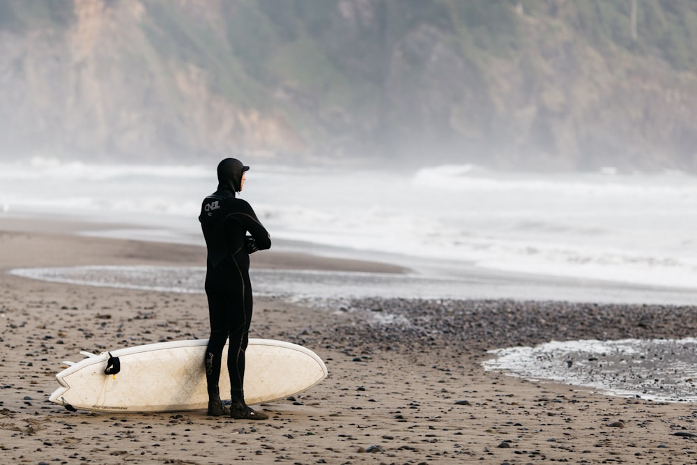 homem em pé na costa com prancha de surf