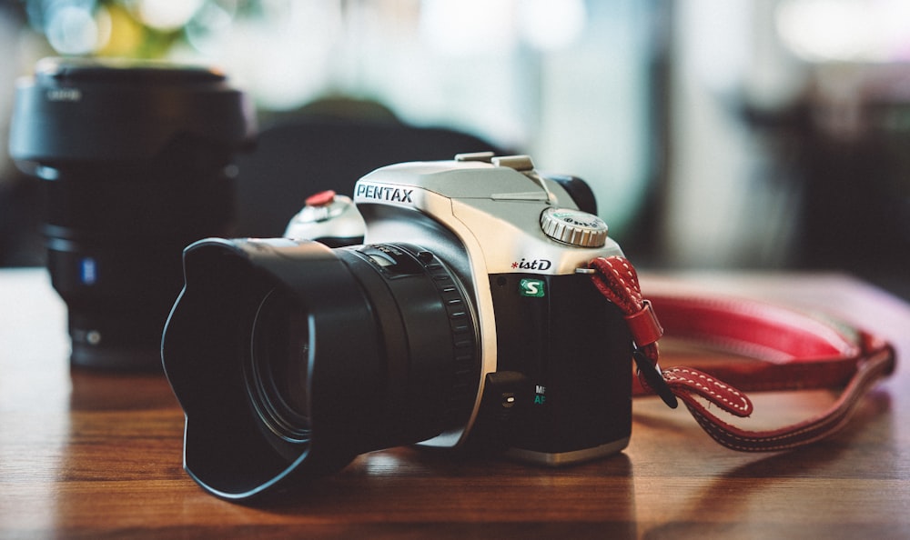 black and gray Pentax DSLR camera on wooden table beside zoom lens