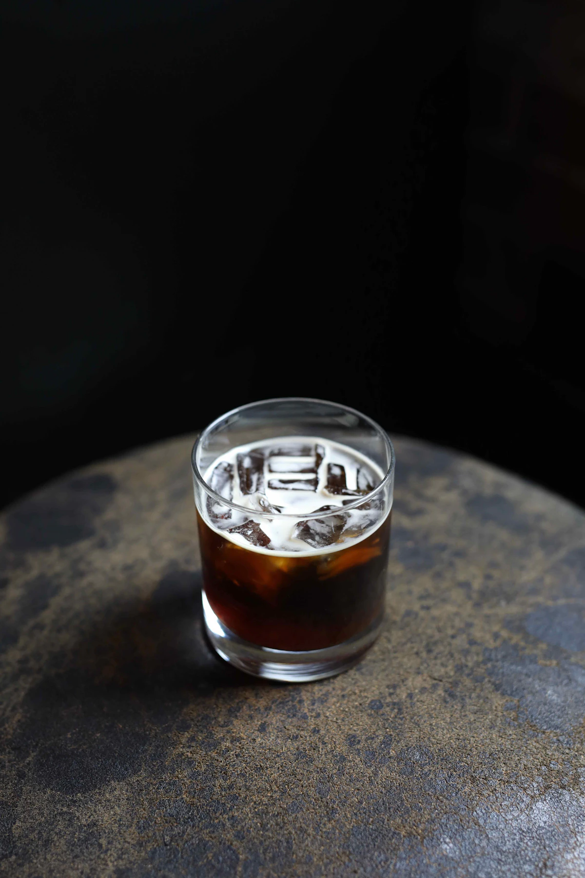 Glass of cold brew iced coffee on a dark stone surface, condensation visible on the outside of the glass