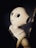 A humanoid robot with large, round eyes and a smooth, white surface is shown. The lighting is dim and casts shadows, highlighting the robot’s sleek and futuristic design.