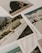 A collection of printed photographs scattered on a surface, with images depicting natural landscapes, including grassy fields and shorelines. The focus is on a photograph featuring a wooden fence alongside green vegetation.