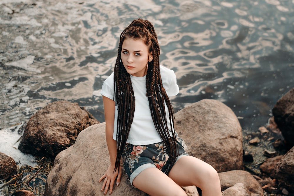 woman sitting on rock formation near body of water