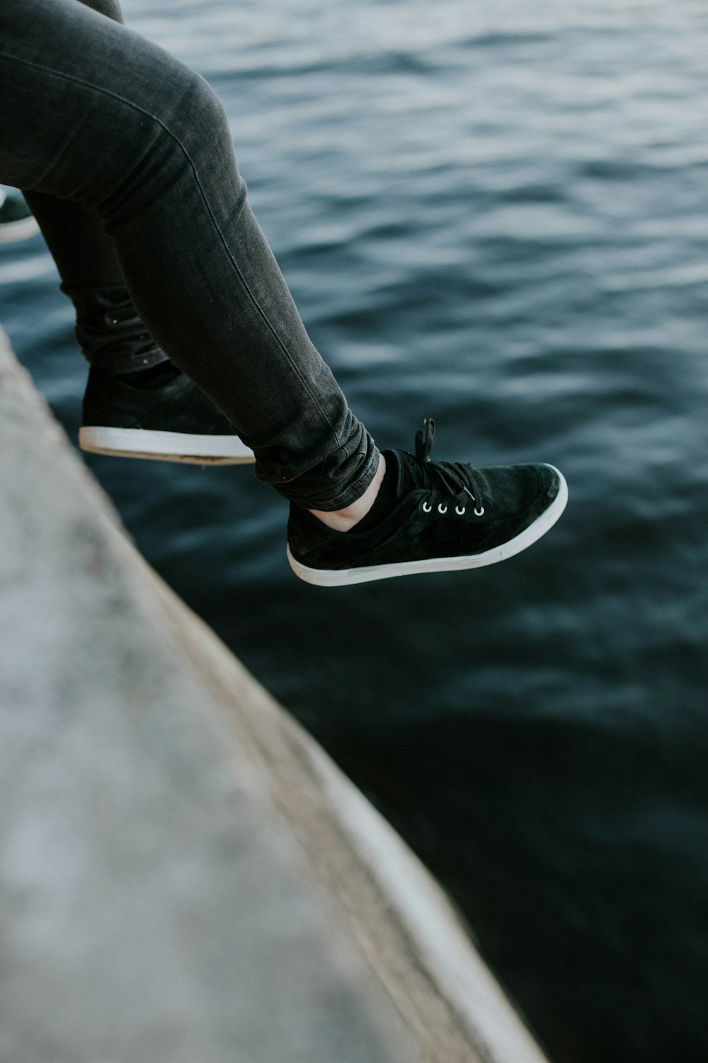 person in black pants sitting on gray concrete surface