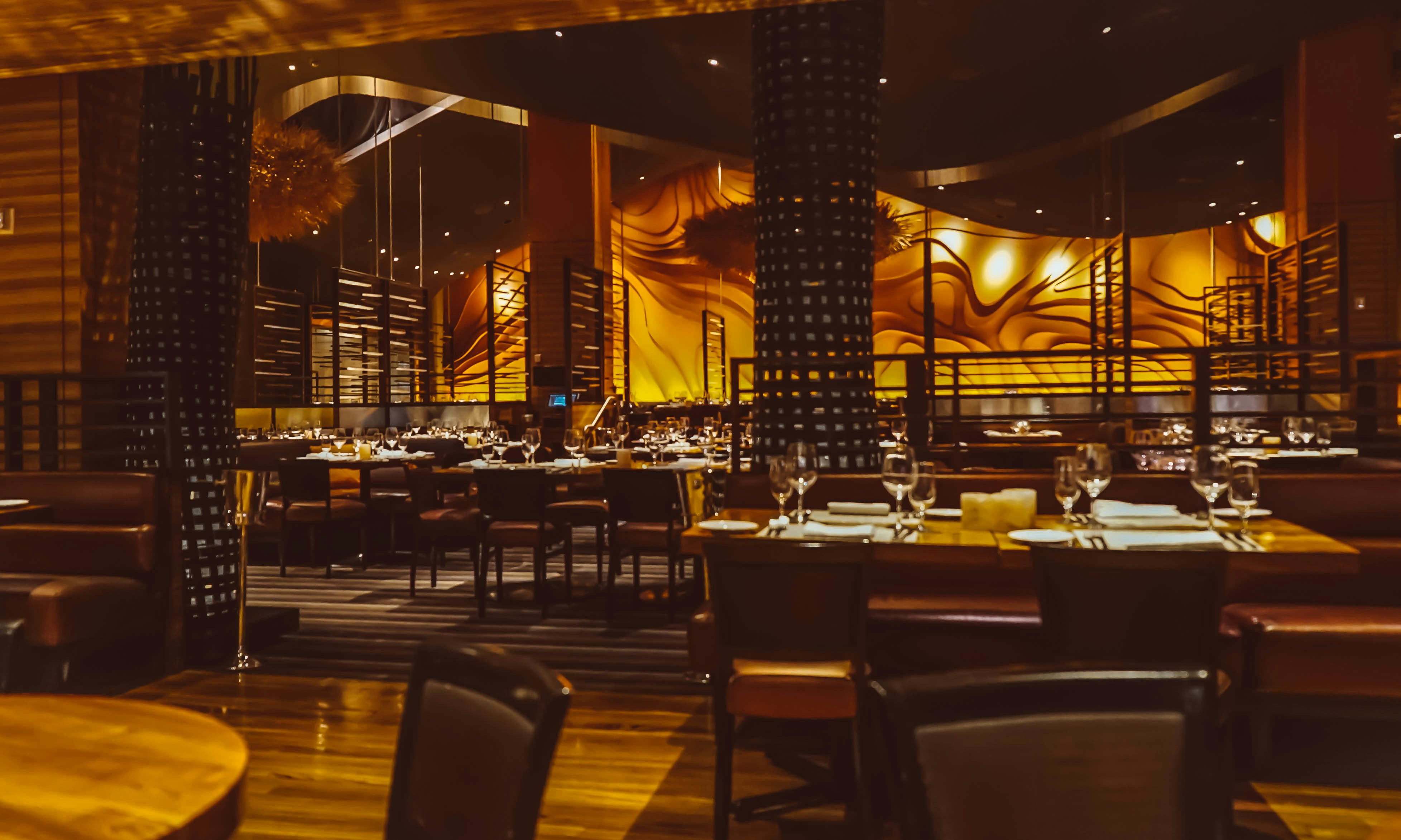 Upscale restaurant dining room with dramatic wood ceiling beams, warm Edison lighting, elegant table settings