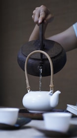 person pouring water on ceramic teapot