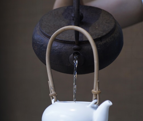 person pouring water on ceramic teapot