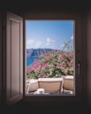 opened window showing outdoor lounger and pink flowers with mountain background