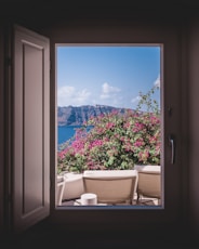 opened window showing outdoor lounger and pink flowers with mountain background