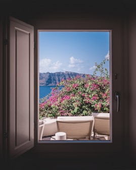 opened window showing outdoor lounger and pink flowers with mountain background