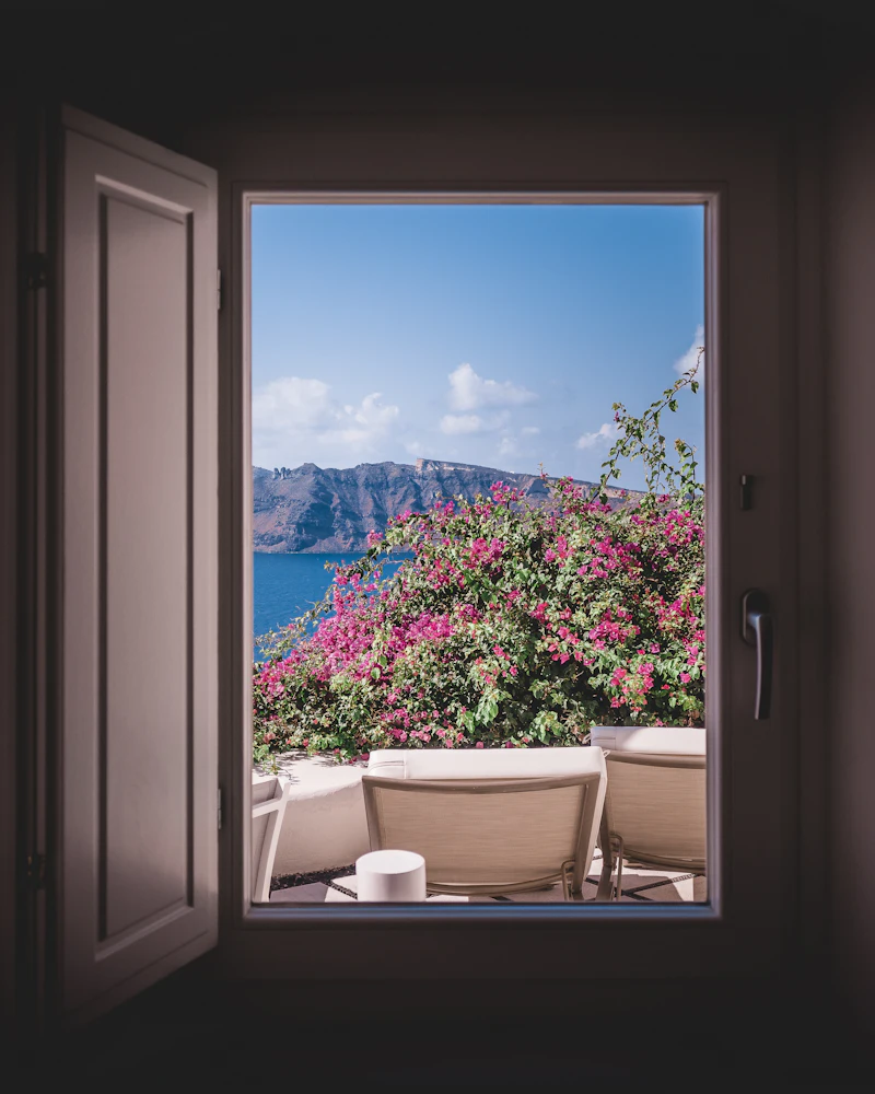 An open wooden window framing pink bougainvillea, a terrace and the caldera