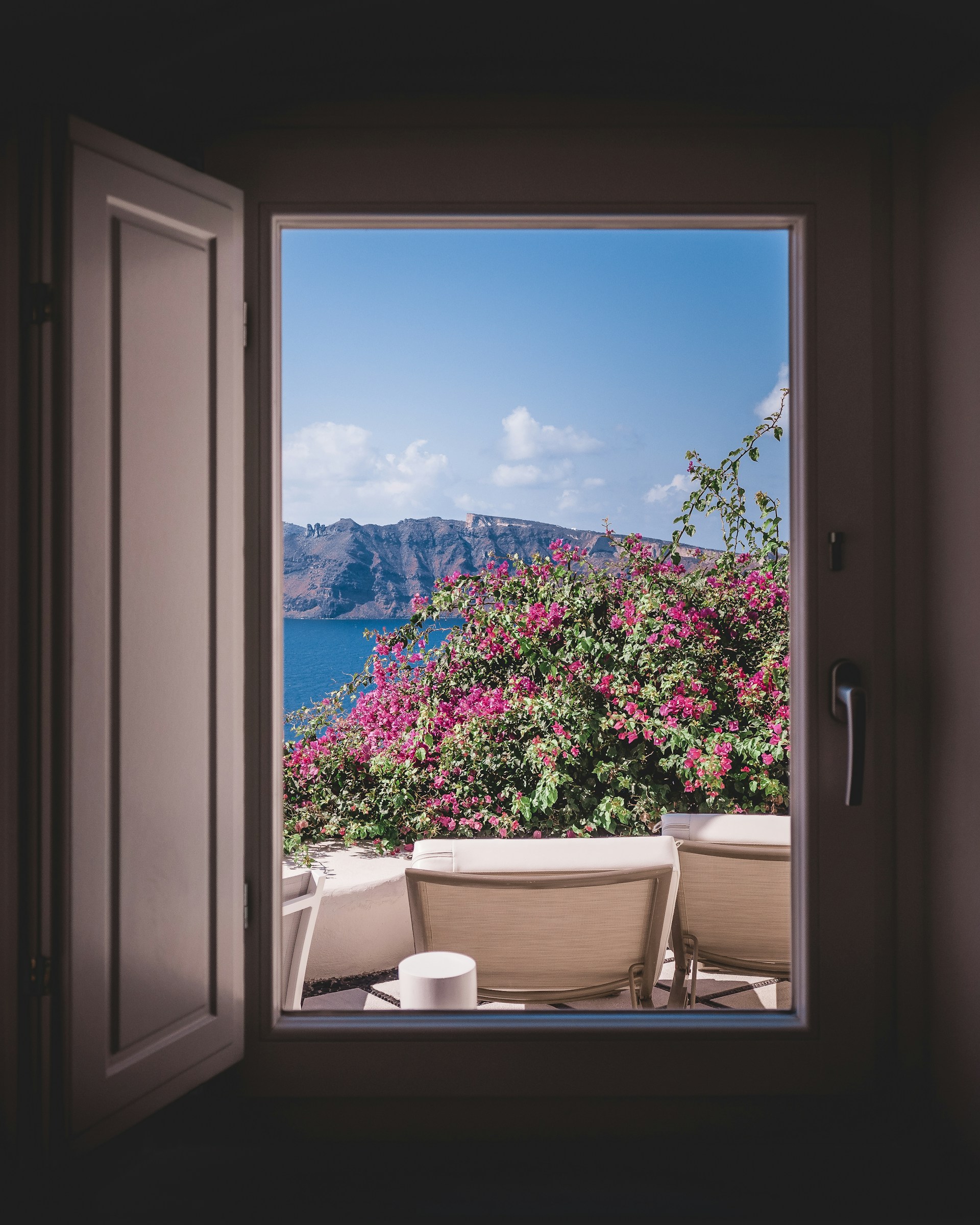 opened window showing outdoor lounger and pink flowers with mountain background