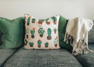 three throw pillows and one white fringed blanket placed on top of gray sofa