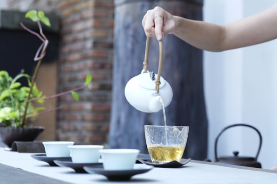 A person holding a kettle, pouring tea into a teacup