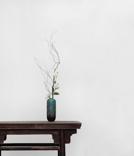 white flowers with green ceramic vase on top of brown wooden side table