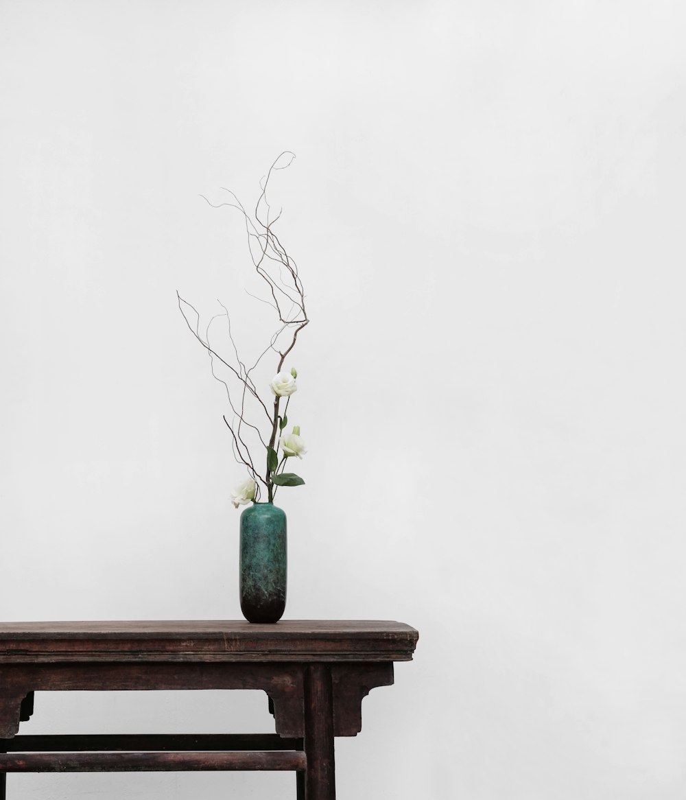 white flowers with green ceramic vase on top of brown wooden side table