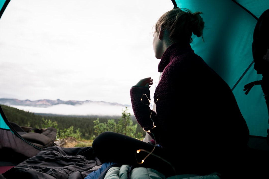 woman sitting inside teal camping tent during daytime