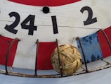A close-up view of a traditional wooden board painted in red, white, and blue with large black numbers (24, 1, 2) displayed. A small wicker ball is placed within a metal cage attached to the board.