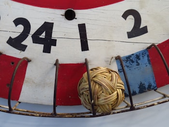 A close-up view of a traditional wooden board painted in red, white, and blue with large black numbers (24, 1, 2) displayed. A small wicker ball is placed within a metal cage attached to the board.