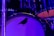 A close-up of a bass drum with a silhouette of a bird on its surface. The drum is part of a larger drum kit and is surrounded by various components, including stands and cymbals. The scene is illuminated with blue and purple lighting, creating a vibrant and atmospheric effect.