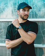 man wearing black crew-neck shirt and black cap in front of glass wall