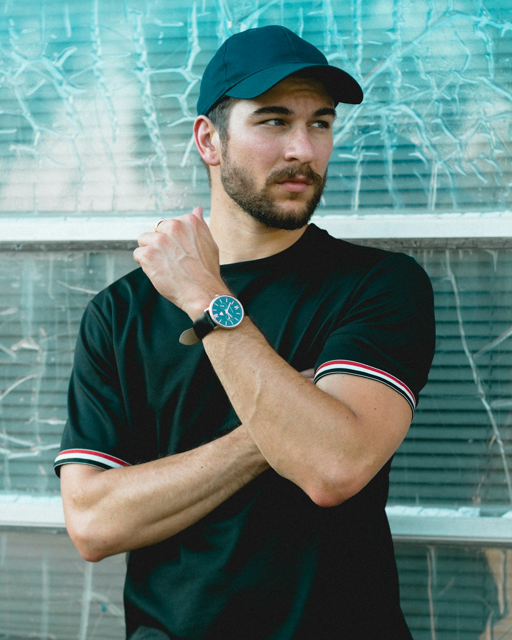 man wearing black crew-neck shirt and black cap in front of glass wall