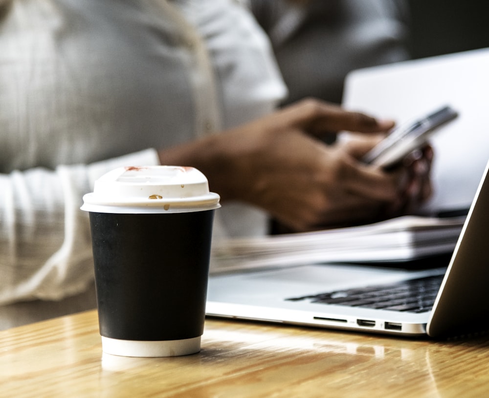 black and white coffee cup beside laptop