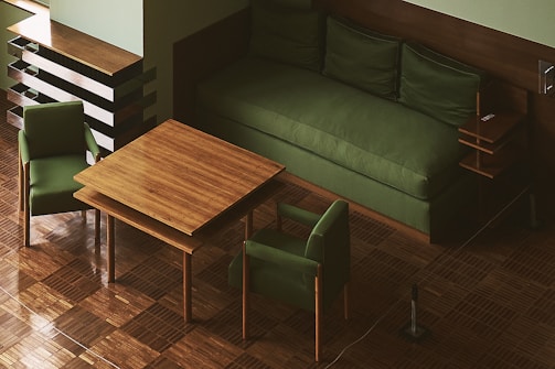 A room with green cushioned furniture including a large sofa and two chairs. The wooden table features a parquet design similar to the flooring. An adjacent modern wooden shelving unit is present.