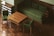 A room with green cushioned furniture including a large sofa and two chairs. The wooden table features a parquet design similar to the flooring. An adjacent modern wooden shelving unit is present.