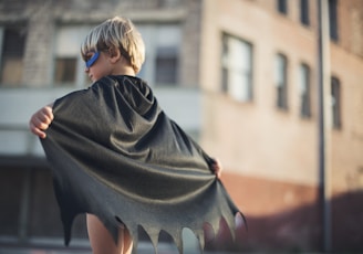 selective focus photography of boy wearing black Batman cape