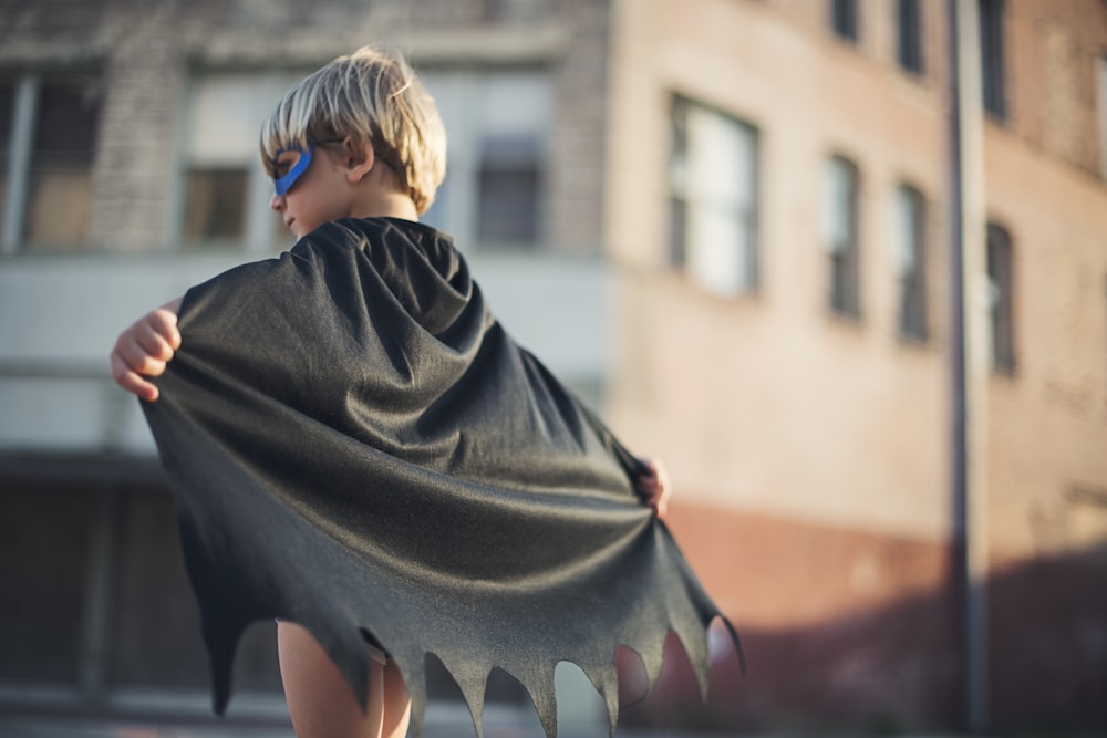 fotografia de foco seletivo do menino vestindo capa preta do Batman