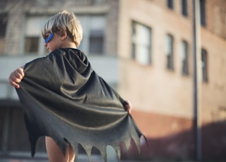 selective focus photography of boy wearing black Batman cape