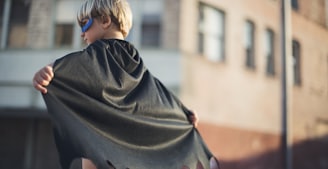 selective focus photography of boy wearing black Batman cape